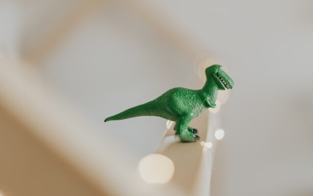 Un Dinosaurio Tiranosaurio Rex de color verde está encima de una barandilla